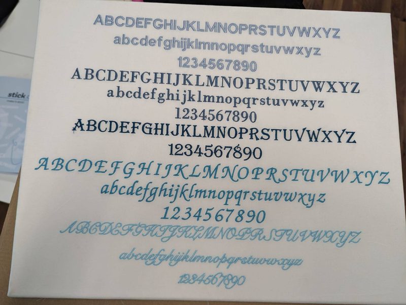 Musterstoff mit fünf gestickten Schriften, Groß- und Kleinbuchstaben und Ziffern in Blautönen